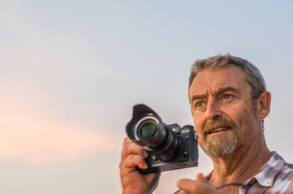 Photographer Mike Browne holding a camera against evening sky
